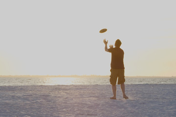 silhouette of a human male boy guy trying to catch a frisbee during sunset at the beach....