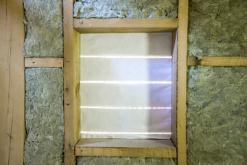 Insulation of attic with fiberglass cold barrier and insulation material. Window in frame wooden house.