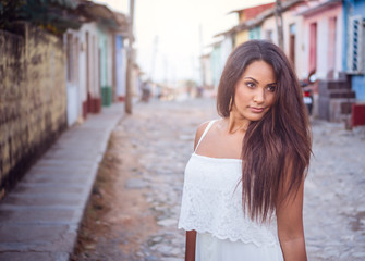Beautiful dark skinned young lady in white dress standing in the old streets of Trinidad in Cuba.
