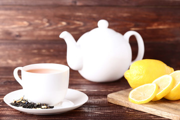 Cup of tea with sliced lemons and teapot on brown wooden table