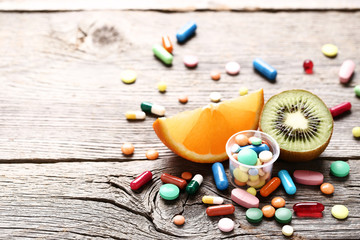 Ripe fruits and colorful pills on wooden table