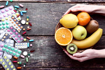 Fototapeta na wymiar Female hands holding ripe fruits in basket and colorful pills on wooden table
