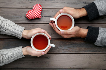 Female and male hand holding cups of tea with fabric heart