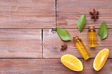 Orange oil in bottles with green leafs and star anise on brown wooden table