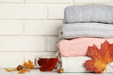 Stack of knitted sweaters with cup of tea and autumn leafs on brick wall background