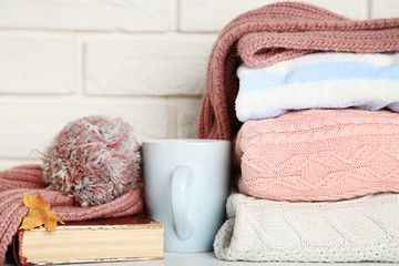 Folded sweaters with cup, scarf and old book on brick wall background