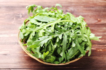 Green arugula leafs in basket on brown wooden table