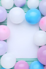 Colorful balloons with sheet of blank paper on wooden table