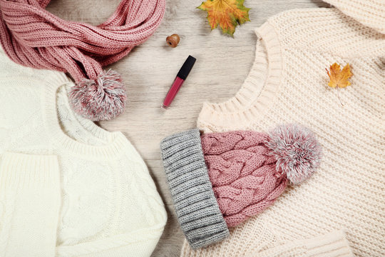 Knitted sweaters with scarf, lip gloss and autumn leafs on the floor