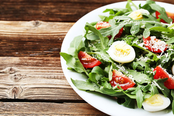 Salad with arugula leafs, tomatoes and eggs on brown wooden table