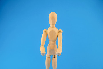 Wooden dummy holds two hands in front of itself on blue background