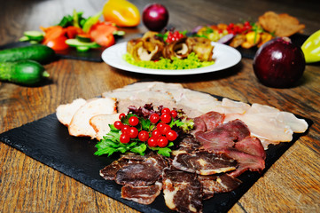 meat slicing of several types of sausage, ham, balyk, pork with red berries close - up on a wooden background. Meat restaurant menu