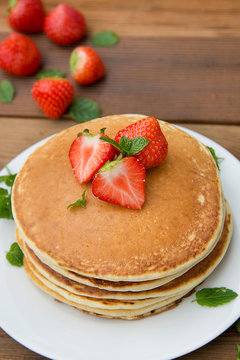 Delicious homemade american pancakes with fresh strawberry and honey. Wooden rustic background. Vertical image, top view.