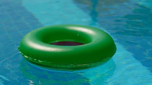 High angle green lifebuoy floating in empty outdoor swimming pool full shot sunlight reflected at pure clean blue water at hot summer day beautiful calm water surface