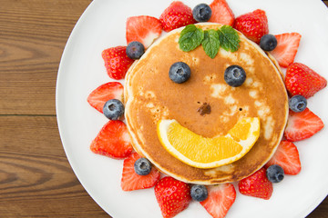 Breakfast for kids. Homemade american pancake sun, with fresh blueberries, strawberries and orange juice. Wooden rustic background.