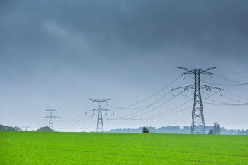 High voltage lines and power pylons in a green agricultural landscape at rainy day with.