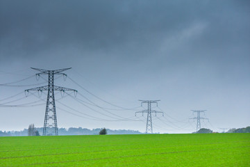 Fototapeta na wymiar High voltage lines and power pylons in a green agricultural landscape at rainy day with.