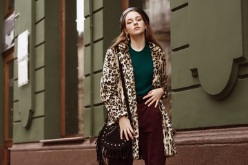 Outdoor fashion portrait of woman wearing trendy animal, leopard print faux fur coat, beret,...