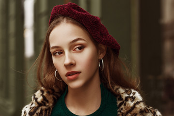 Outdoor close up fashion portrait of young beautiful confident woman wearing marsala color beret,...
