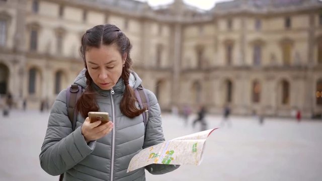 Lost female tourist using two maps two find a way in new city, woman googling sightseeing in Paris.