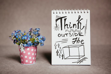Think outside the box - business quote on white paper with blue flowers, calligraphy text