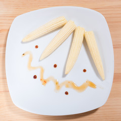 raw cob mini corn on a plate decorated with sauce. Square photo format