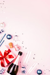 Christmas gift with red bow, bottle of champagne, two glasses and blue decorationson pink background. Beautiful holiday composition. Vertical background with copy space.