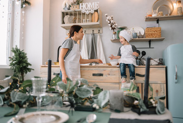 Young happy mom and her baby cook cookies at home in the kitchen. Christmas Homemade Gingerbread. cute boy with mother in white uniform and hat cooked chocolate cookies