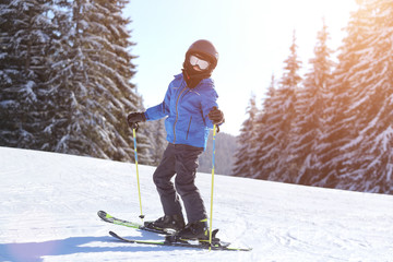 Fototapeta na wymiar Small boy skiing on slope at mountain ski resort