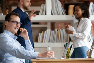Smiling confident businessman talking by phone at shared workplace, mobile with client, customer,...