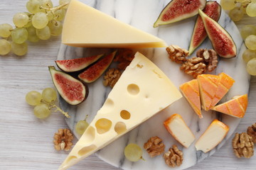 Three types of cheese and fruit on a marble board. Aged Cheese, Maasdam and Soft Cheese with red rind