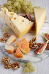 Three types of cheese and fruit on a marble board. Aged Cheese, Maasdam and Soft Cheese with red rind