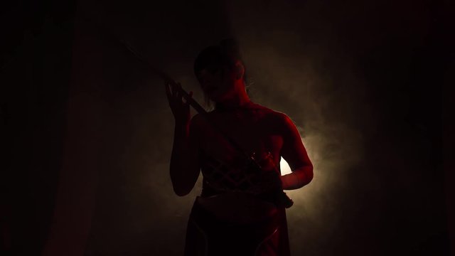 the attractive girl stands in a room with dim light and fog, her red silhouette perfectly conveys her movements, the samurai truly admires the new sword, studies it with a look, holds it in her hands