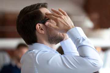 Stressed exhausted businessman massaging temples after working long hours with computer, documents,...