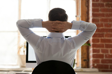 Relaxing businessman stretching with hands behind head after long work in sitting position with...