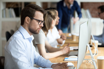 Obraz premium Serious focused businessman looking at monitor screen, employee doing difficult online work, using computer, applications , typing business email, writing economic report, perform task