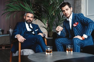Men with a great style. Two young handsome men in suits looking at camera while resting indoors.