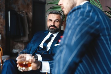 Relaxing. Full length of two young handsome men in suits holding glasses and looking at each other...