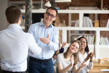 Middle aged happy smiling boss, mentor congratulating employee, praise for good work, new project, idea for startup, shaking hand, welcoming new member of business team, colleagues applauding