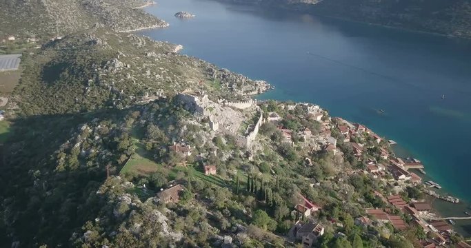 Point of interest aerial drone footage orbit left around Simena Castle ruins, Kalekoy village with Kekova Island coast background in Turkey. 4k at 23.97fps