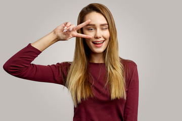 Funny positive girl shows peace sign. Beautiful girl having fun indoors isolated on white background. The concept of body language