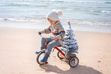 Santa claus kid in Christmas sweater. Happy child on the bicycle or tricycle near water. Xmas party...