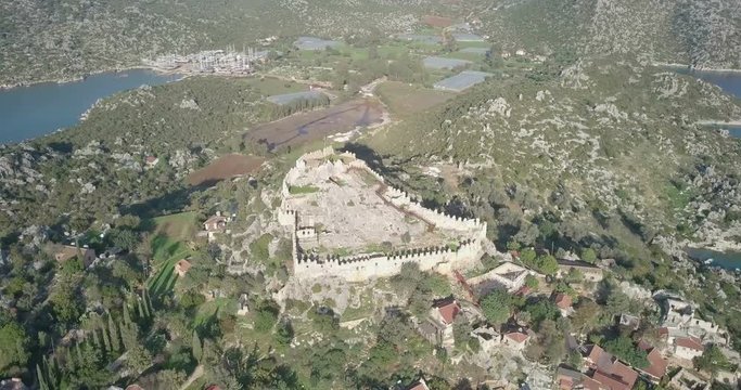 Aerial drone footage orbit right around Simena Castle, necropolis, and Kalekoy Village with Ucagiz village background in Turkey. 4k at 23.97fps