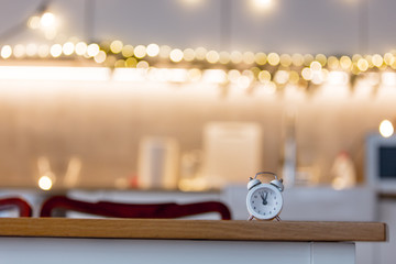 little alarm clock on a table with Christmas lights on background. Kitchen interior