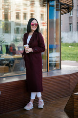 Outdoors lifestyle fashion portrait of stunning brunette girl. Smiling, drinking coffee and walking...