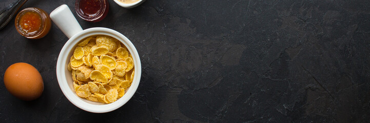 cornflakes, coffee, cottage cheese, bread, butter, eggs, jam and other ingredients for breakfast on a dark background. Top view with copy space