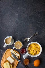 cornflakes, coffee, cottage cheese, bread, butter, eggs, jam and other ingredients for breakfast on a dark background. Top view with copy space