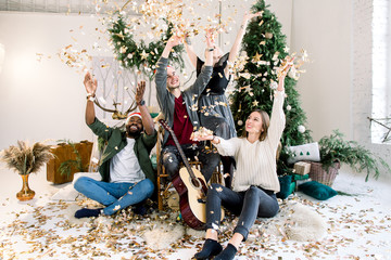 Group of smiling international friends having fun with confetti flappers. People are sitting at...