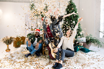 Concept of Christmas holidays and New Year party. Four multiracial friends celebrating Christmas in...