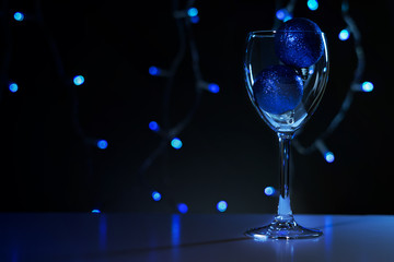 Christmas cards. Wine glass with red, blue and gold Christmas decorations on dark background with christmas tree garland.